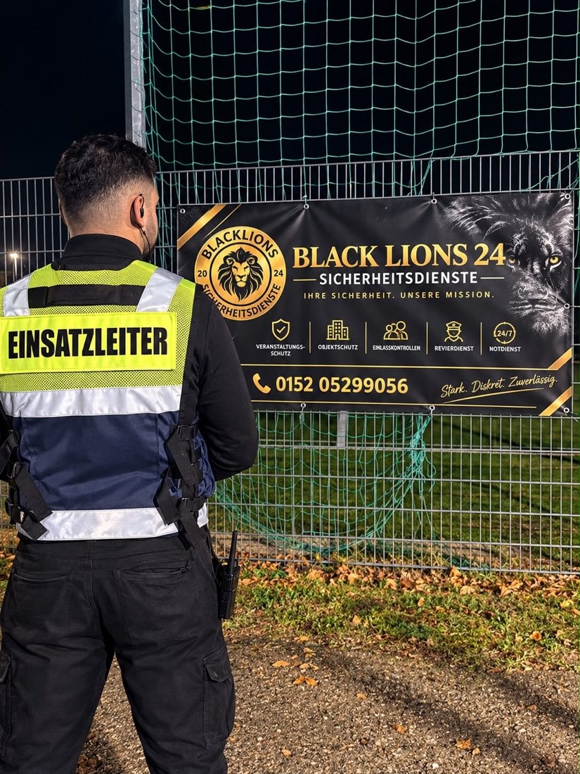 Einsatzleiter von Black Lions 24 am Sportplatz vor dem Firmenbanner